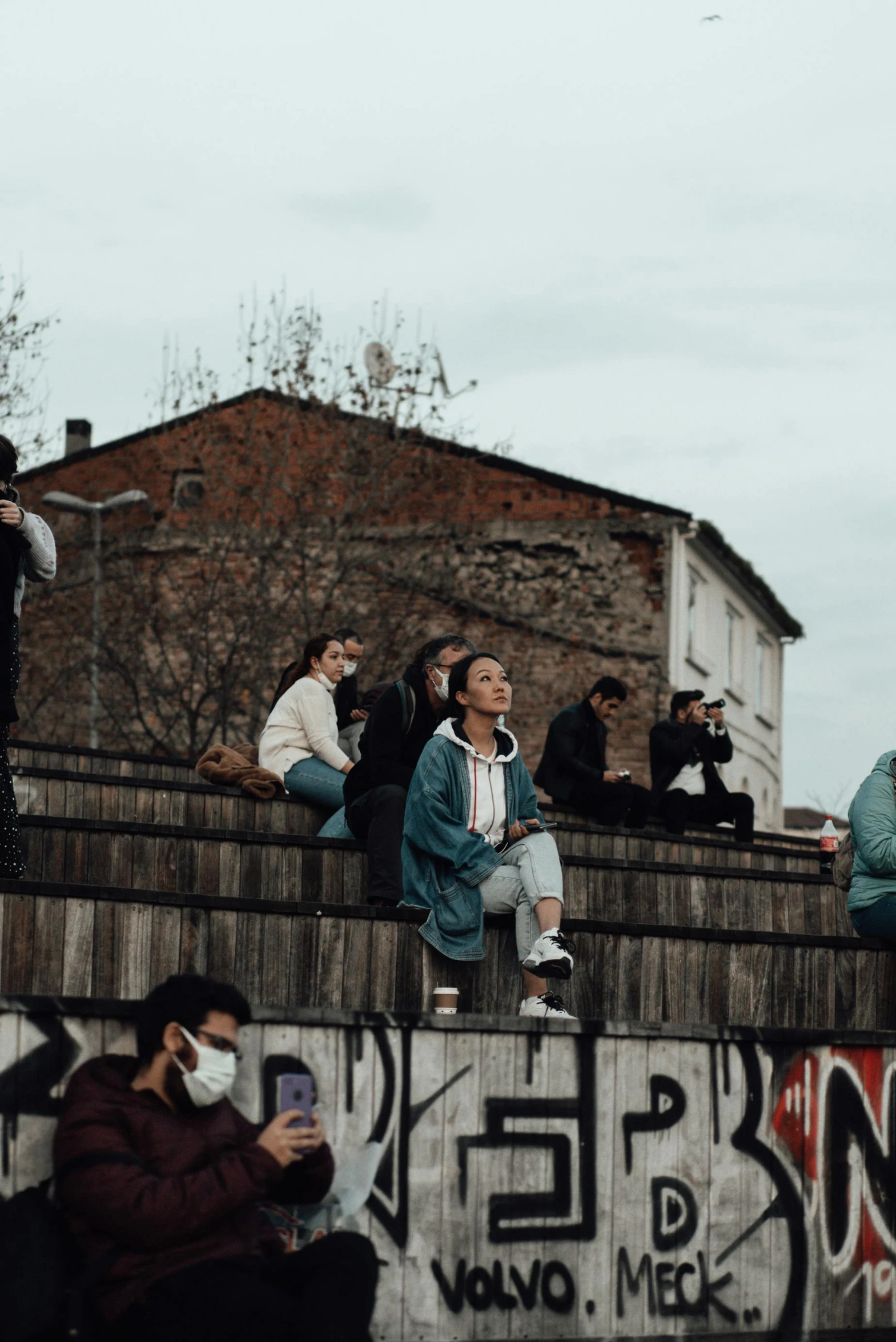 a group of people sitting on top of a wall, trending on pexels, graffiti, audience in the background, romanian, 😭 🤮 💕 🎀, human staring blankly ahead