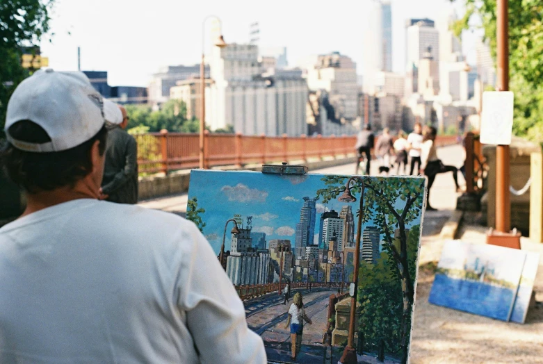 a man that is standing in front of a painting, by William Berra, pexels contest winner, plein air, on a bridge, minneapolis, painting a canvas, view from the streets