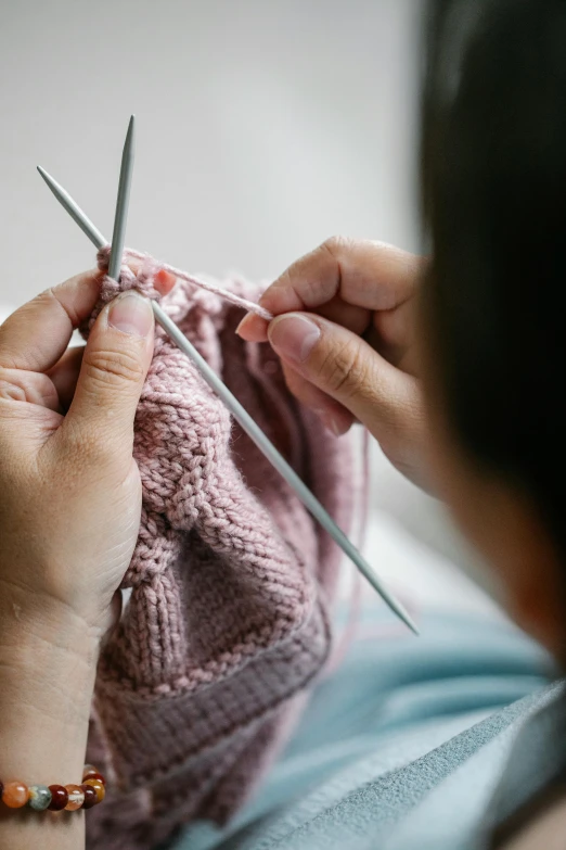 a woman knitting with a pair of knitting needles, by Julian Allen, pexels, process art, wearing a pink hoodie, creating a soft, technical, children's