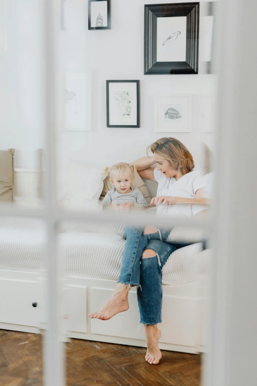 a woman sitting on top of a white couch next to a little girl, pexels contest winner, looking through a window frame, jeans and t shirt, a blond, product introduction photo