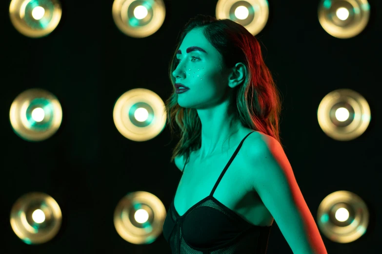 a woman standing in front of a wall of lights, trending on pexels, lily collins, blue and green light, natalia dyer, ( ( stage lights ) )