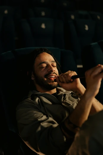 a man sitting in a theater looking at his cell phone, pexels contest winner, jesus christ smoking a blunt, laughing, cinematic lut, holding microphone