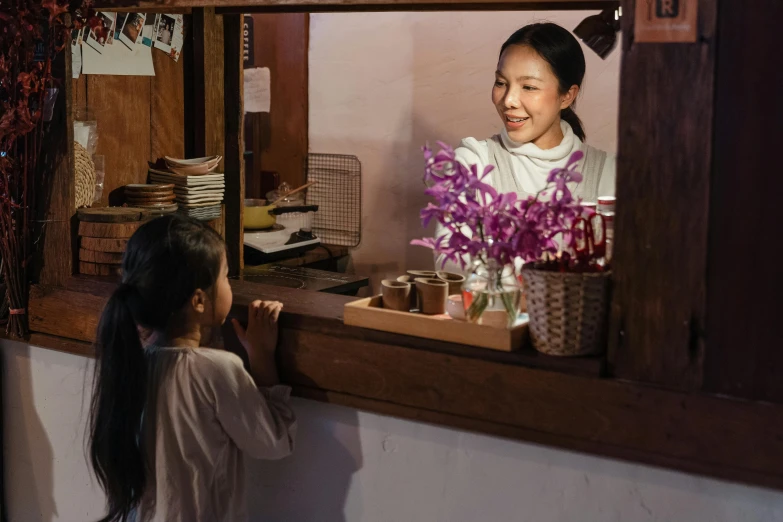 a woman standing at a counter in front of a mirror, inspired by Jiao Bingzhen, pexels contest winner, with a kid, flower shop scene, award winning movie still, caretaker