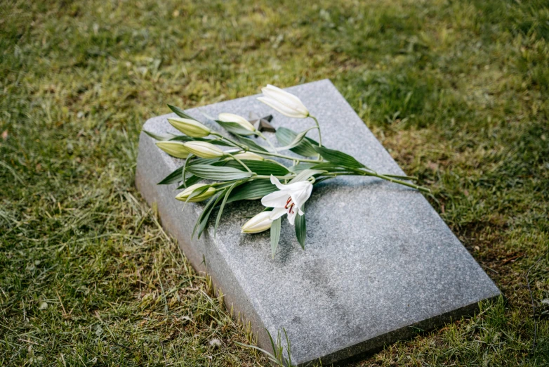 a grave with a bunch of flowers on top of it, unsplash, realism, white lilies, granite, rectangular, grey