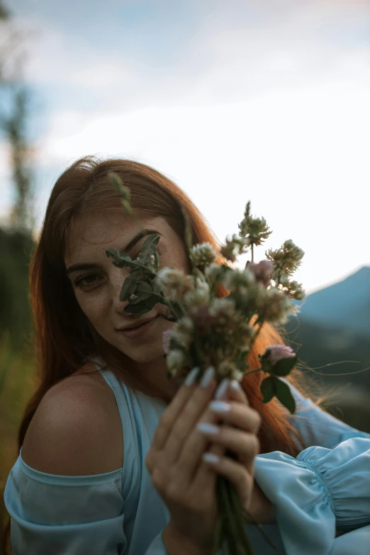a woman in a blue dress holding a bunch of flowers, a picture, inspired by Elsa Bleda, pexels contest winner, red haired young woman, a mountain look like a women, flowers and butterflies, smug look