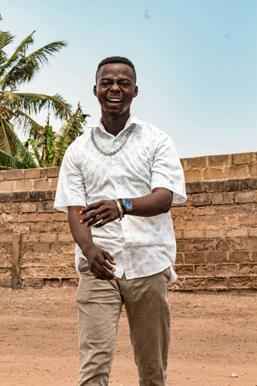 a man standing in front of a brick wall, happening, in africa, wearing a shirt, smiling male, wearing a white shirt