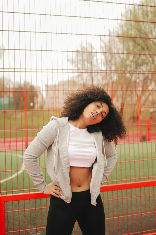 a woman standing in front of a fence with her hands on her hips, pexels contest winner, happening, curls on top, sports setting, mixed race woman, 15081959 21121991 01012000 4k