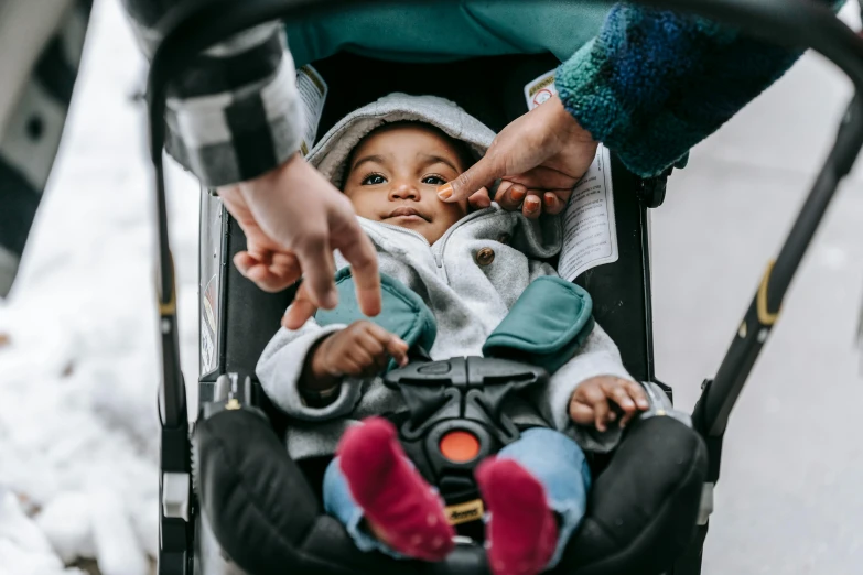 a person pushing a baby in a stroller, by Nina Hamnett, pexels contest winner, kid named finger, varying ethnicities, looking up at camera, panel of black