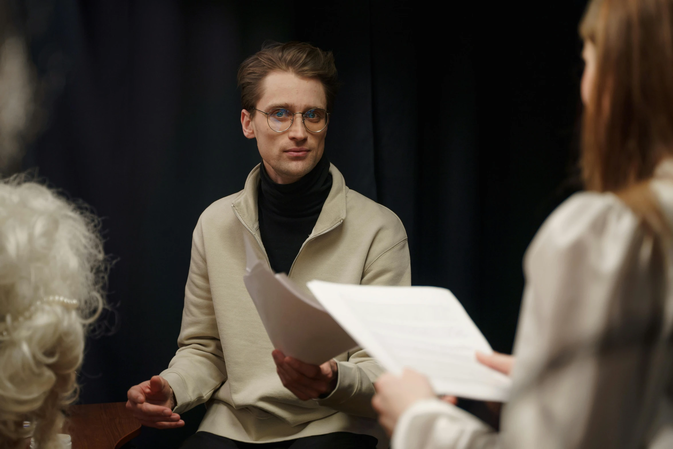 a man sitting in a chair talking to a woman, by László Balogh, reddit, performance, he is wearing a brown sweater, high quality photo, androgynous person