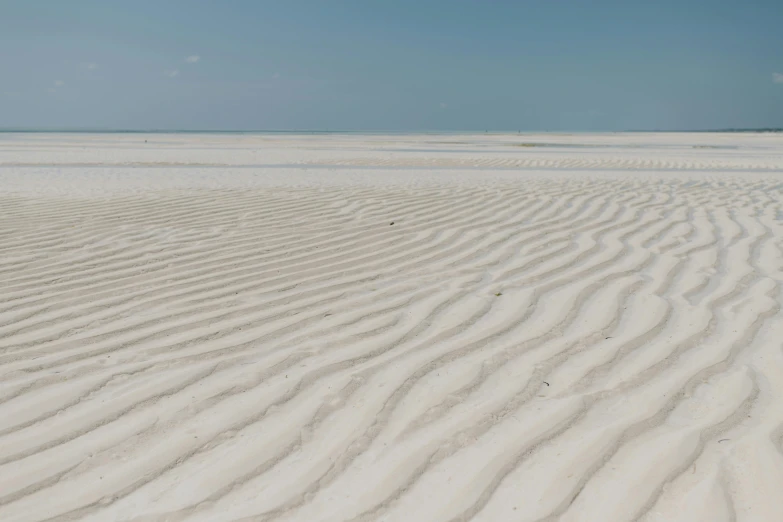 a man riding a surfboard on top of a sandy beach, by Andries Stock, unsplash contest winner, minimalism, rippled white landscape, somalia, extremely detailed sand, infinite intricacy