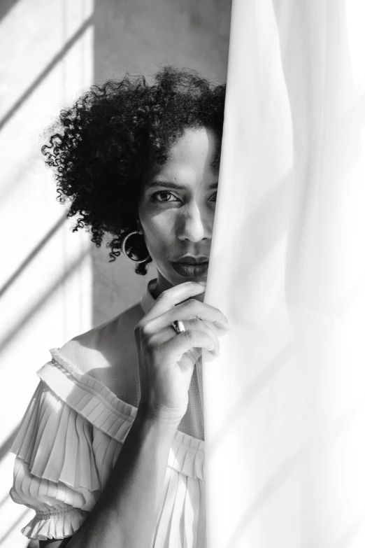 a black and white photo of a woman peeking out of a curtain, inspired by Carrie Mae Weems, short black curly hair, square, transparent background, sunshine light