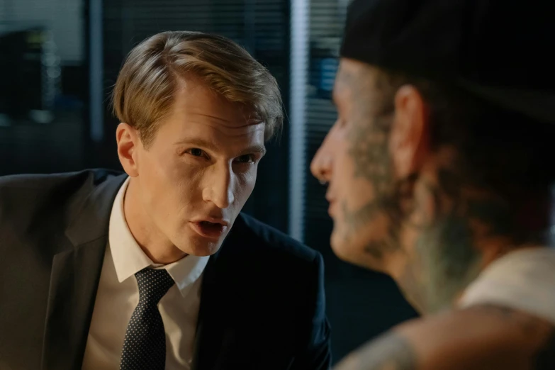 a man in a suit and tie talking to another man, a tattoo, felix englund, worksafe. cinematic, liam brazier, holding court
