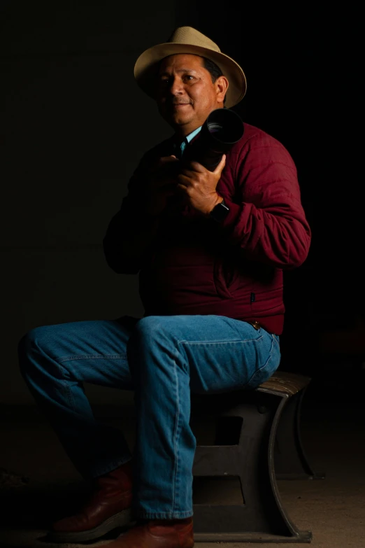 a man sitting on a stool holding a camera, george strait, 7 0 mm dramatic lighting, eloy morales, profile picture