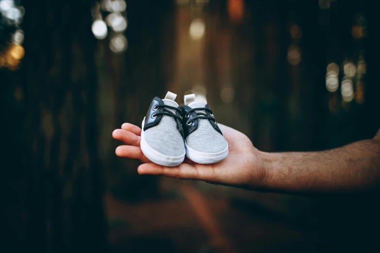 a person holding a pair of shoes in their hand, by Romain brook, pexels contest winner, third trimester, with a tree in the background, boys, avatar image