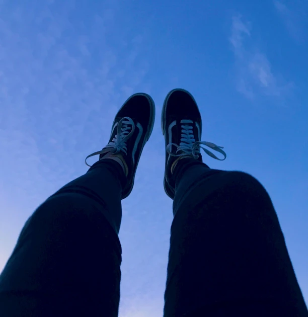 a person standing on top of a skateboard under a blue sky, black shoes, low light, childhood friend vibes, viewed from the ground