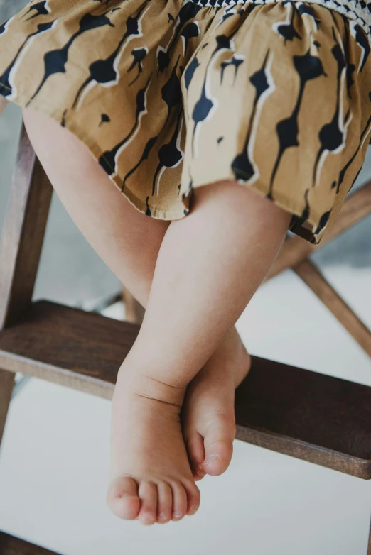 a baby sitting on top of a wooden step stool, trending on unsplash, patterned clothing, black fine lines on warm brown, close-up on legs, the dress\'s lower