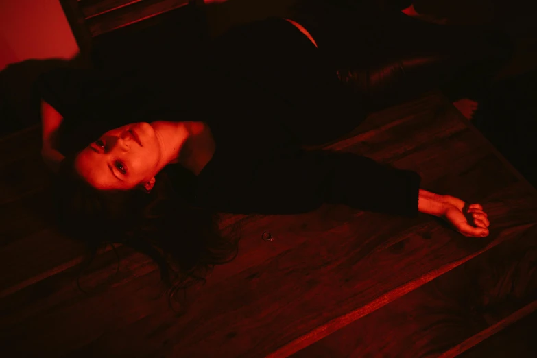 a woman laying on the floor in a dark room, with red haze, dark clothing, head tilted down, red room