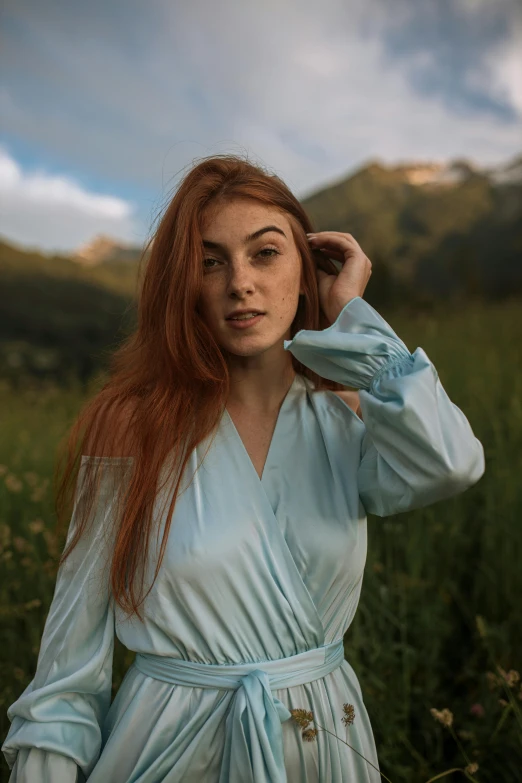a woman in a blue dress standing in a field, a portrait, inspired by Elsa Bleda, pexels contest winner, renaissance, copper hair, wearing a light blue shirt, with mountains as background, 🤤 girl portrait