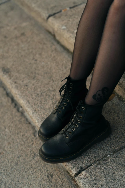 a close up of a person sitting on some steps, an album cover, inspired by Elsa Bleda, trending on pexels, graffiti, doc marten boots, 1 7 - year - old goth girl, leather stockings, closeup - view