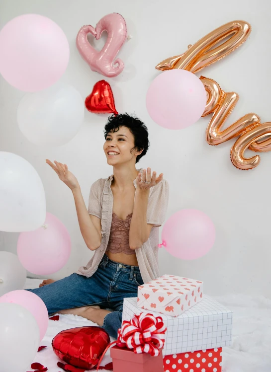 a woman sitting on a bed surrounded by balloons, happening, pink hearts in the background, curated collections, on simple background, holding gift