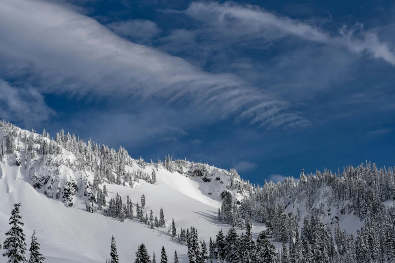 a man riding a snowboard down the side of a snow covered slope, a photo, unsplash contest winner, precisionism, strange trees and clouds, black fir, cirrus clouds, conde nast traveler photo