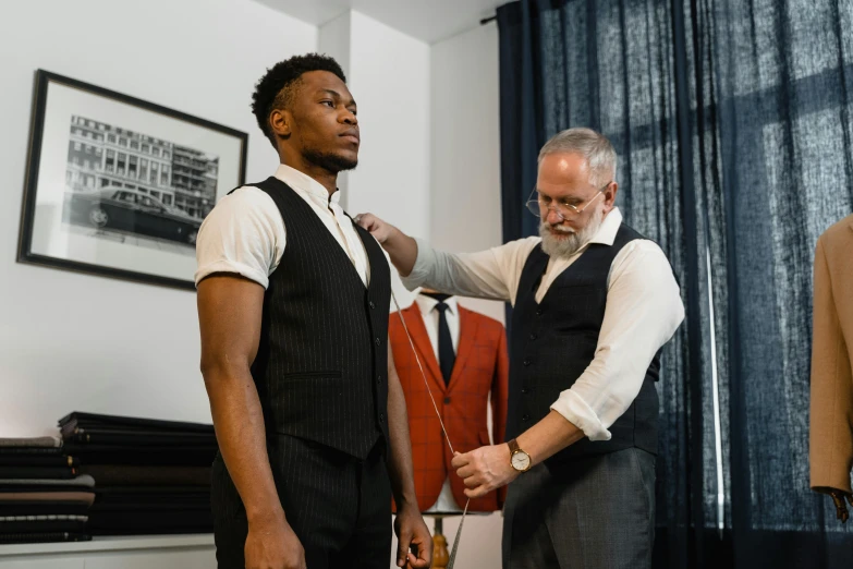 a man putting a tie on another man's neck, pexels contest winner, vests and corsets, wearing track and field suit, inspect in inventory image, man is with black skin