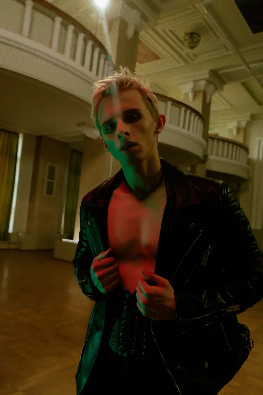 a man that is standing in a room, inspired by Nan Goldin, trending on pexels, bauhaus, dressed in punk clothing, pale hair, hero pose colorful city lighting, jacket over bare torso