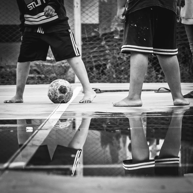 a group of young men playing a game of soccer, a black and white photo, by Joze Ciuha, pexels contest winner, realism, water reflection on the floor, hd footage, kids playing, portrait of a big