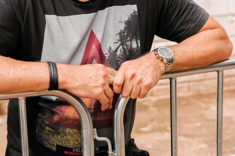 a man standing next to a metal fence, a tattoo, trending on pexels, sitting in a wheelchair, bracelets, wearing a t-shirt, watch photo