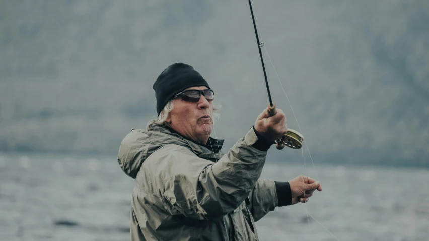 a man holding a fishing rod next to a body of water, a picture, ian callum, flying towards the camera, enjoying the wind, pekka halonen