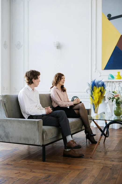 two people sitting on a couch in a living room, by Maud Naftel, pexels contest winner, visual art, in a meeting room, sitting with flowers, looking serious, man and woman walking together