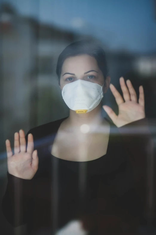 a woman wearing a face mask looking out a window, a picture, hands shielding face, square, worksafe. cinematic, biohazard