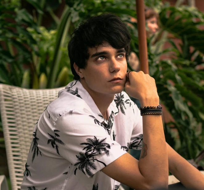 a man sitting at a table with a laptop, an album cover, inspired by John Luke, pexels contest winner, with palm trees in the back, whitebangsblackhair, patterned clothing, closeup portrait shot