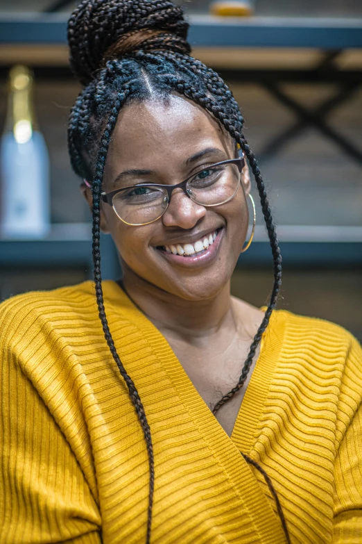 a smiling woman wearing glasses and a yellow sweater, by Lily Delissa Joseph, black hair in braids, background bar, full frame image, portrait n - 9