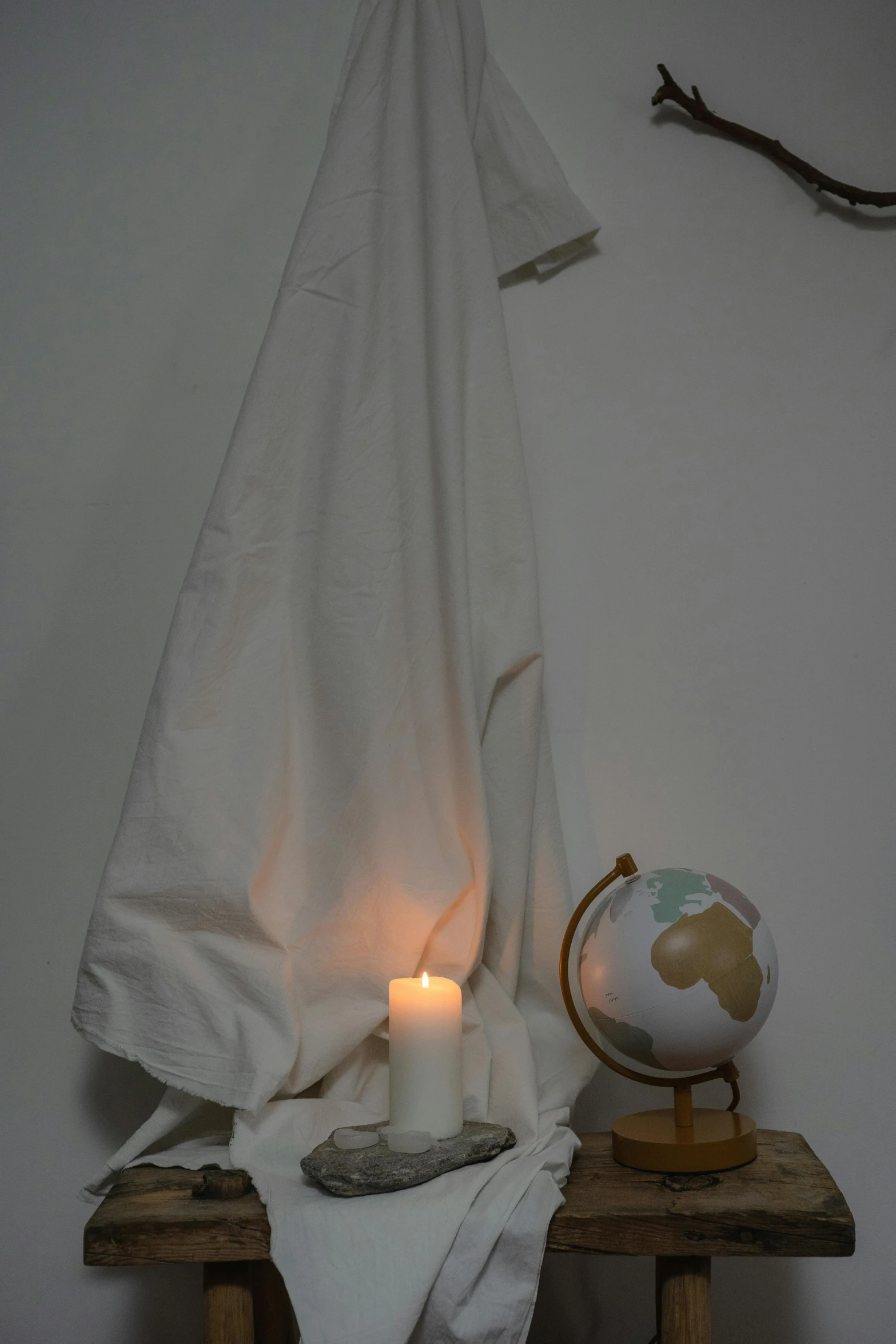a white towel sitting on top of a wooden table, a statue, holding a candle, with earth, light clothing, softlight