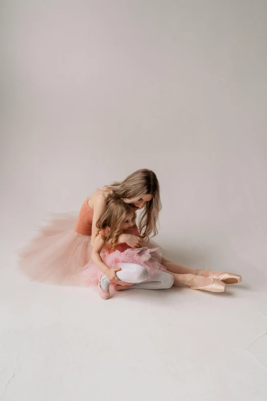 a little girl in a pink dress sitting on the floor, a picture, by Ruth Simpson, trending on pexels, arabesque, woman holding another woman, lois greenfield, creating a soft, ellie victoria gale