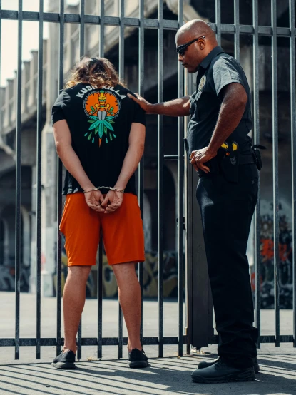 a couple of people that are standing in front of a fence, by Jacob Toorenvliet, wearing a marijuana t - shirt, black and orange, arrested, 🚿🗝📝