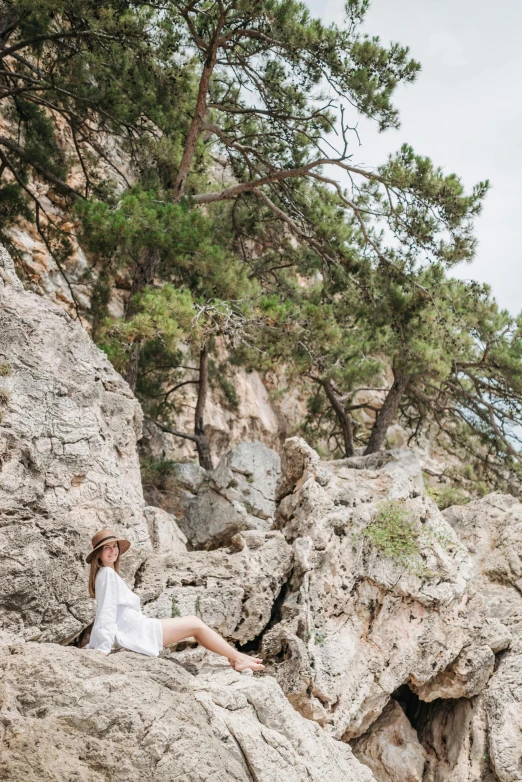 a woman sitting on top of a large rock, capri coast, dressed in white robes, solo hiking in mountains trees, rocky beach