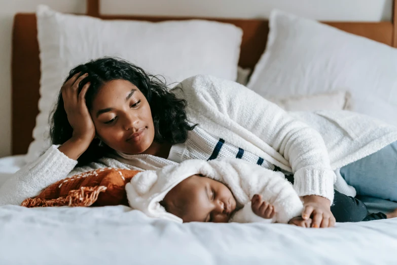 a woman laying on top of a bed next to a baby, pexels contest winner, diverse, cuddling, profile image, thumbnail