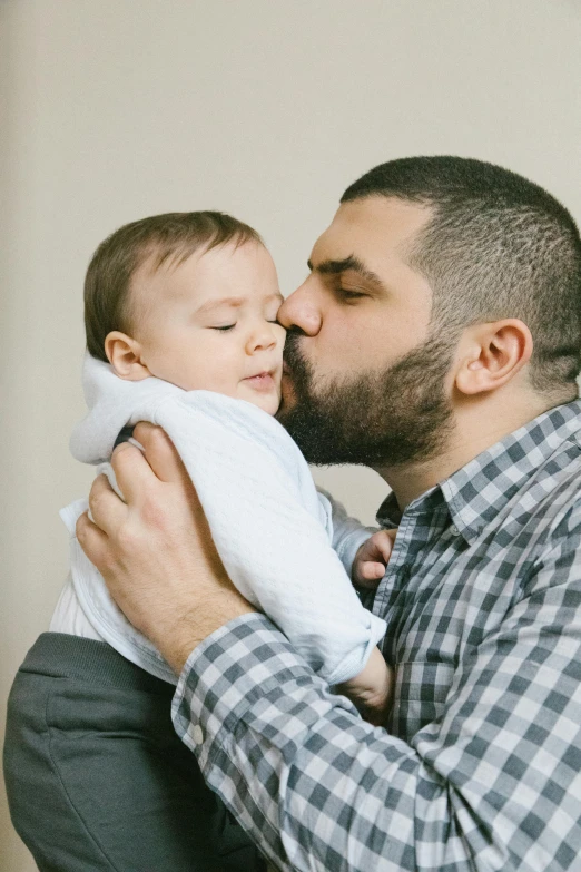 a man holding a baby in his arms, a colorized photo, shutterstock contest winner, beard stubble, kissing each other, zachary quinto, portrait featured on unsplash