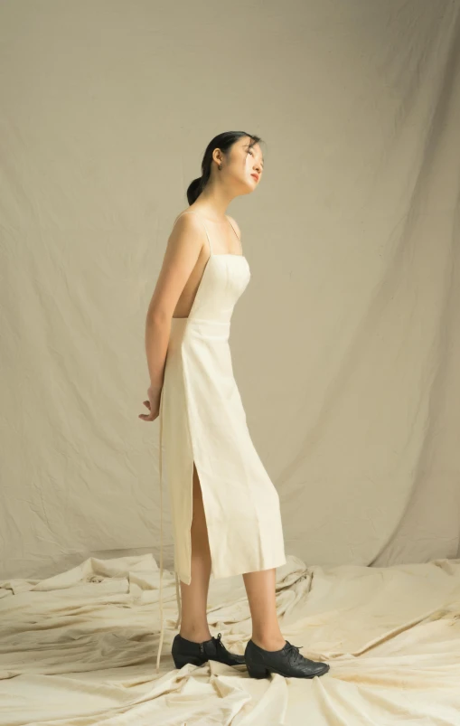 a woman in a white dress standing on a sheet, an album cover, inspired by Tang Di, unsplash, official store photo, long dress with apron, back slit, wearing ivory colour dress