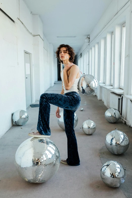 a woman sitting on top of a silver ball, by Matija Jama, trending on pexels, arabesque, androgynous male, wearing pants, flares, standing