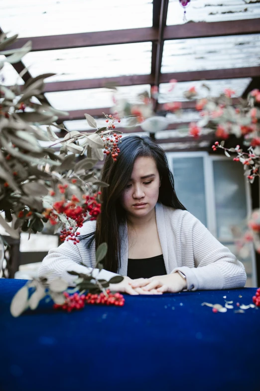 a woman sitting at a table with berries on it, by Julia Pishtar, pexels contest winner, process art, young asian woman, heartbroken, holiday season, covered with flowers