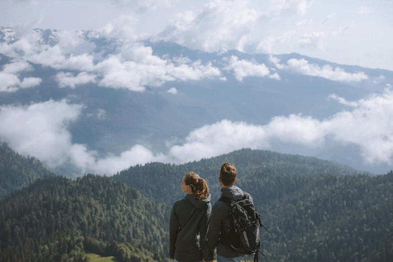 a couple of people standing on top of a mountain, by Emma Andijewska, pexels contest winner, overlooking a vast serene forest, clouds visible, profile image, birdseye view