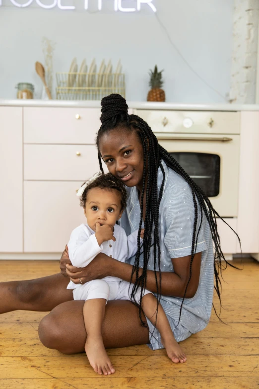 a woman sitting on the floor holding a baby, by Lily Delissa Joseph, pexels contest winner, in the kitchen, light-brown skin, on clear background, ikea