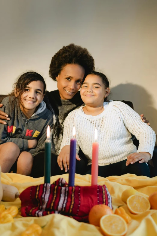 a woman and two children sitting on a bed with candles, lgbtq, aida muluneh, holiday season, slide show