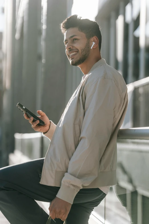 a man sitting on a ledge using a cell phone, trending on pexels, wearing a track suit, lean man with light tan skin, smiling male, integrated synthetic android