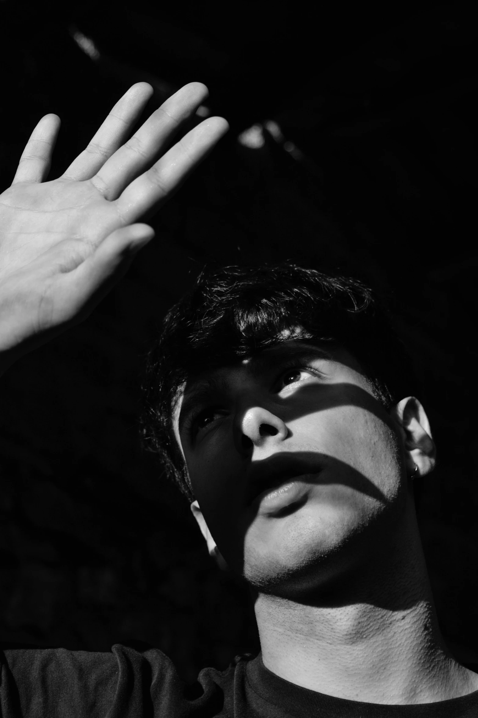 a black and white photo of a man with his hands in the air, a black and white photo, by Alexis Grimou, cheekbones, blindfold, declan mckenna, the sun is blinding