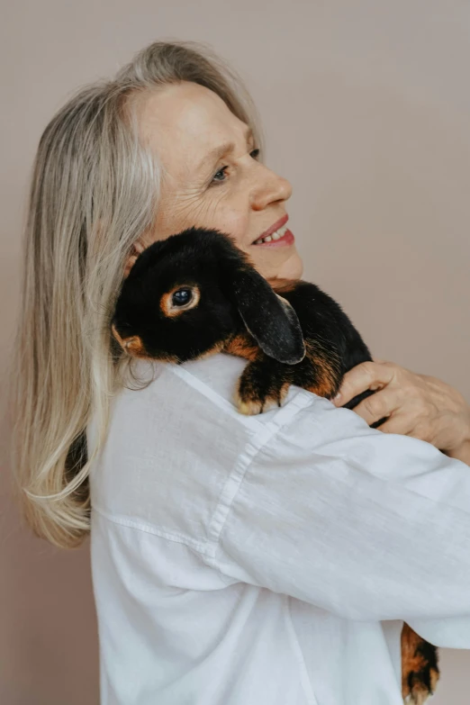 a woman in a white shirt holding a black and brown dog, by Elizabeth Durack, pexels contest winner, with bunny rabbit ears, older woman, plushie, enamel