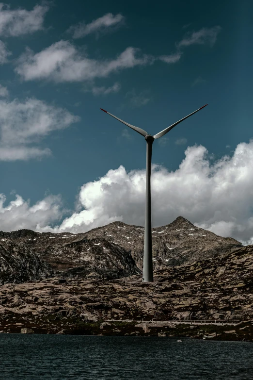 a wind turbine on top of a mountain next to a body of water, a portrait, unsplash contest winner, grey, carbon, 360 foot wingspan, on ground